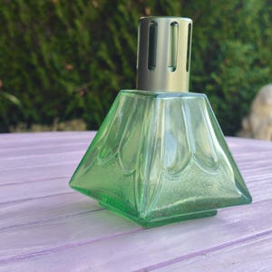 May include: A square-based green glass fragrance lamp with a translucent finish and a molded petal pattern on the sides. The vessel features a metallic silver-toned vented cap at the top, designed for air purification and scent diffusion.