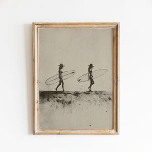 May include: A framed wall art print featuring a sepia-toned illustration of two figures wearing hats and carrying surfboards. The artwork has a distressed, grainy texture with dark ink splatters across the bottom and a light beige background.