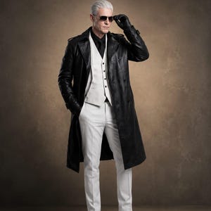 Könnte beinhalten: Ein schwarzer Ledertrenchcoat über einer weißen Weste, weißen Hose und einem schwarzen Hemd. Das Outfit umfasst schwarze Lederhandschuhe, schwarze Lederstiefel und dunkel getönte Sonnenbrillen. Das Ensemble zeichnet sich durch einen strukturierten Kragen aus.