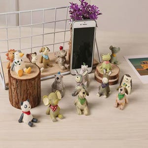 Puede incluir: Una colección de pequeñas figuras de animales pintadas a mano, incluyendo un panda, un elefante, un burro, una rana y un perro, cada uno con un pañuelo colorido. El conjunto presenta varias criaturas como un león, un mono y un erizo.