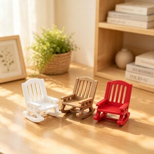 Puede incluir: Tres mecedoras en miniatura dispuestas en fila, que incluyen una blanca, una de madera marrón claro natural y una de color rojo brillante. Cada silla tiene un respaldo de listones, reposabrazos y balancines curvos en la base.