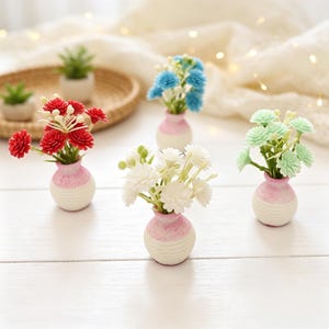 Puede incluir: Cuatro jarrones decorativos en miniatura, cada uno con un pequeño ramo de flores artificiales. Los jarrones tienen una forma redondeada con una parte superior texturizada de color rosa y una base blanca acanalada. Las flores son rojas, azules, blancas y verde claro.