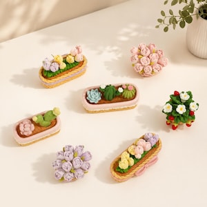 Puede incluir: Una colección de siete artículos decorativos en miniatura con diversos arreglos florales y de suculentas. Se incluyen macetas ovaladas con flores y cactus en tonos pastel, una planta de fresas con flores blancas y dos ramos redondos de rosas moradas y rosas.