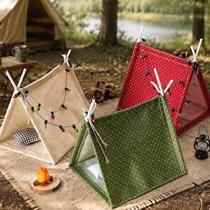 Puede incluir: Tres tiendas de campaña en miniatura con forma de A en tela color crema, roja y verde con lunares blancos. Cada tienda cuenta con postes de soporte blancos, una cadena de luces decorativas multicolores y un pequeño cojín interior. Incluye una fogata y una linterna en miniatura.