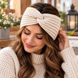 May include: A cream-colored crochet headband featuring a central twist detail. The accessory is crafted with a textured, ribbed stitch pattern that covers the ears and forehead, providing a thick, warm appearance with a consistent knit construction.