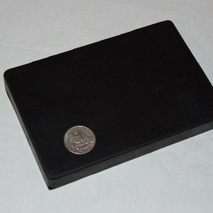 May include: A black rectangular box with a coin on top. The coin is silver and has a design on it.