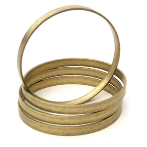 May include: A stack of thin, gold-colored metal bangles. The bangles are circular and appear to be made of a flat metal strip. The image is set against a white background.