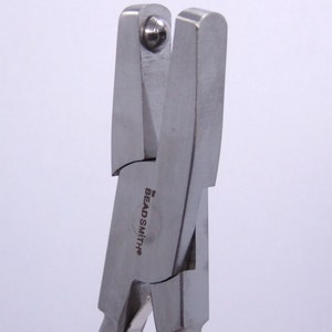 May include: Close-up of a silver beadsmith pliers with a rounded tip. The pliers are designed for crimping beads and have a logo that reads "Beadsmith".