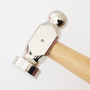 May include: A silver metal hammer with a wooden handle. The hammer has a round head and a flat face.