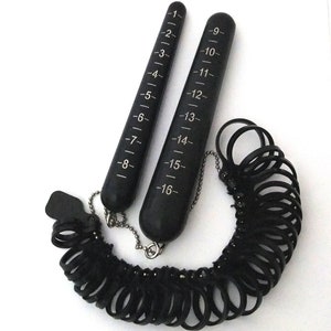 Op de afbeelding: Een zwarte ringmaatset met twee meetstokken en een ketting van plastic ringmaten. De stokken zijn gemarkeerd met nummers van 1 tot 16.