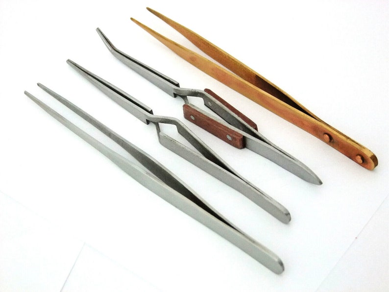 May include: Four tweezers, two with wooden handles, one with a brass finish, and one with a silver finish.