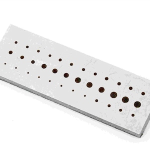 Può includere: Un blocco rettangolare di legno grigio chiaro con una serie di fori circolari marrone scuro di varie dimensioni. I fori sono disposti in un motivo a griglia sulla superficie del blocco. Il blocco è leggermente inclinato.