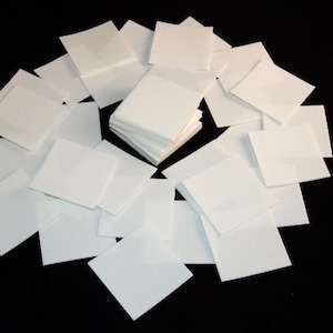 May include: A stack of white square paper napkins arranged in a circle on a black background.