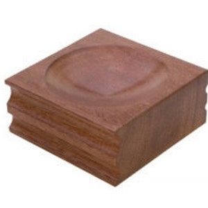 May include: A wooden block with a rounded indentation in the centre. The block is made of reddish-brown wood and has a smooth, polished finish.