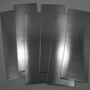 May include: A stack of six rectangular sheets of silver metal.