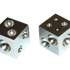 May include: Two silver metal blocks with rounded indentations on each side. The blocks are used for shaping metal.