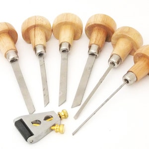 Könnte beinhalten: Satz mit sieben Holzgriff-Schnitzwerkzeugen aus Metall mit einem Schleifwerkzeug aus Metall. Die Werkzeuge haben unterschiedlich geformte Klingen zum Schnitzen von Holz.