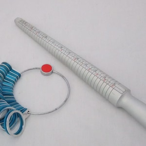 May include: A silver ring sizer with a blue and silver ring gauge. The ring sizer has a red knob on the end.