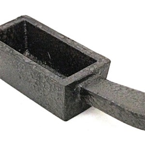 May include: A black cast iron ingot mould with a handle. The mould is designed to create rectangular bars of metal.