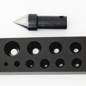 May include: A black metal block with ten different sized holes and a metal pointed tool.
