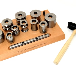 May include: A 10-piece bangle forming dies set with a wooden base and a black rubber mallet. The dies are made of metal and are arranged in a row on the base. The mallet has a wooden handle.
