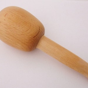 Könnte beinhalten: Ein Holzhammer mit einem runden Kopf und einem langen Stiel. Der Hammer ist aus hellbraunem Holz gefertigt und hat eine glatte Oberfläche.