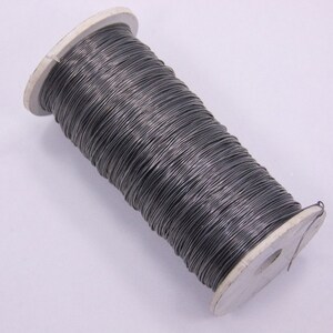 May include: A spool of silver-colored wire wrapped around a white cardboard spool.