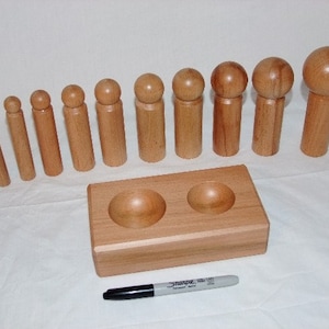 May include: A set of 10 wooden dowels with rounded tops, ranging in size, and a wooden base with two depressions. The dowels are used for a craft project.