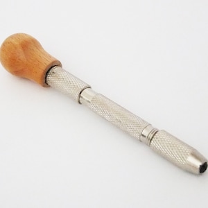 May include: A silver and wood tool with a wooden handle and a metal shaft. The shaft has a textured surface and a pointed tip.