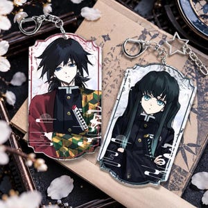 May include: Two rectangular acrylic keychains featuring anime-style characters. The left keychain shows a character with black hair in a red and green patterned haori. The right keychain depicts a character with long black hair in a black uniform.