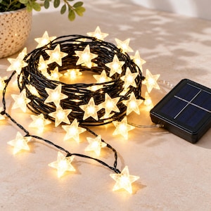 May include: A string of solar-powered LED lights featuring translucent star-shaped covers that emit a warm glow. The lights are connected by a thin black wire and include a rectangular black solar panel module attached to the end of the cord.