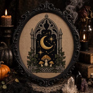 May include: A cross-stitch embroidery in an oval black frame featuring a gothic archway, a golden crescent moon, and stars against a dark background. Below the arch, three mushrooms are surrounded by green vines on a tan fabric background.