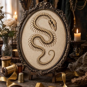 May include: An oval-framed embroidery piece featuring a detailed golden-brown skeletal snake design stitched onto a light beige fabric. The ornate, dark metallic frame surrounds the needlework, which depicts the winding spine and skull of a serpent.