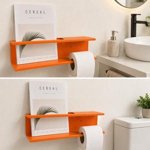 Puede incluir: Un estante de pared de color naranja brillante con una superficie superior plana y una sección inferior diseñada para sostener un rollo de papel higiénico. Una revista titulada CEREAL con un gráfico de hoja de palma descansa sobre el estante.