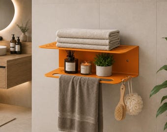 Puede incluir: Un estante de baño de metal montado en la pared de color naranja brillante con dos niveles. El nivel superior sostiene tres toallas beige dobladas. El nivel inferior sostiene un difusor de varillas, una vela en un frasco de vidrio y una planta.