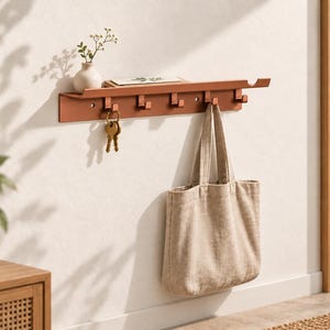 May include: A wall-mounted metal coat rack in a matte terracotta finish featuring a narrow top shelf and five square hooks. The rack holds a beige canvas tote bag and a set of brass keys hanging from one of the hooks, with a small vase on the shelf.