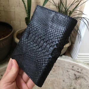 以下が含まれることがあります： 表面全体に独特の隆起した鱗模様が施された、長方形の黒い財布。この財布は構造化された折りたたみ式のデザインで、一貫した暗い色調の仕上げと、エキゾチックな革の質感に特徴的な繰り返しのパターンが施されています。