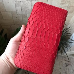 Peut inclure: Un portefeuille rectangulaire dot&eacute; d'un ext&eacute;rieur rouge vif avec une texture en &eacute;cailles en relief. Le portefeuille pr&eacute;sente une fermeture &eacute;clair sur tout le pourtour avec une tirette en m&eacute;tal argent&eacute; dans le coin inf&eacute;rieur.