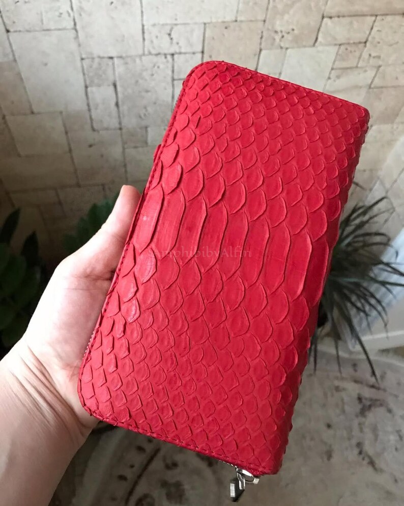 Peut inclure: Un portefeuille rectangulaire dot&eacute; d'un ext&eacute;rieur rouge vif avec une texture en &eacute;cailles en relief. Le portefeuille pr&eacute;sente une fermeture &eacute;clair sur tout le pourtour avec une tirette en m&eacute;tal argent&eacute; dans le coin inf&eacute;rieur.