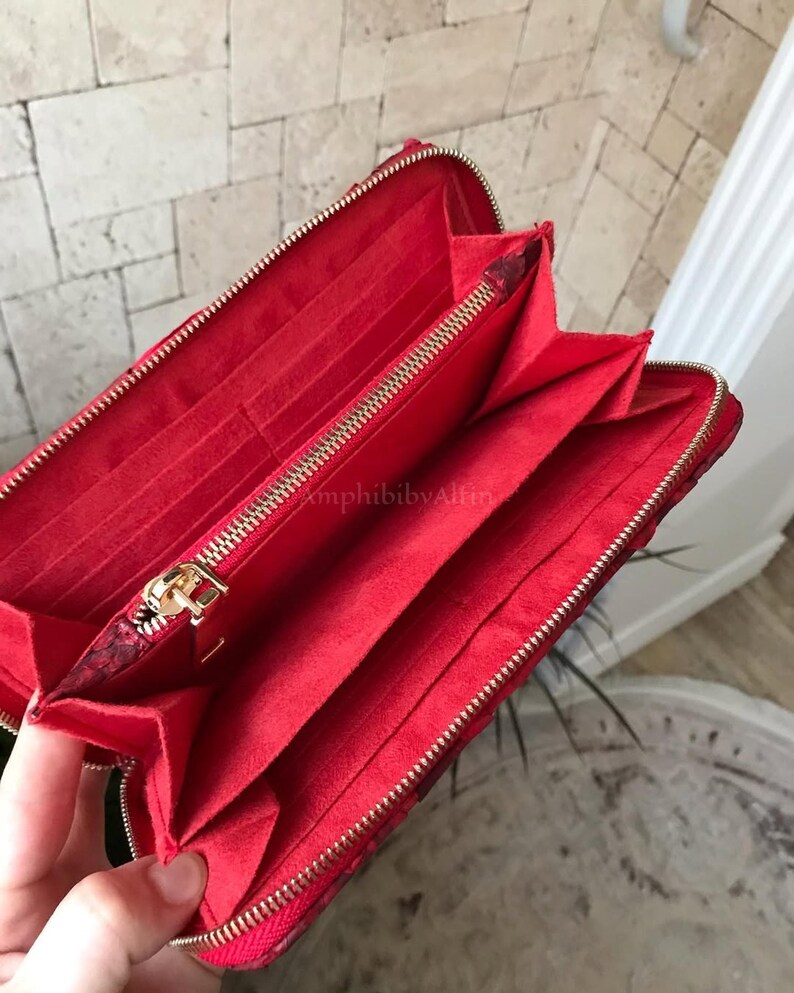 Peut inclure: Un portefeuille rouge avec un ext&eacute;rieur textur&eacute; et une fermeture &eacute;clair dor&eacute;e. L'int&eacute;rieur est doubl&eacute; de tissu rouge et comprend plusieurs fentes pour cartes, un compartiment central zipp&eacute; et des sections ouvertes pour organiser les billets.