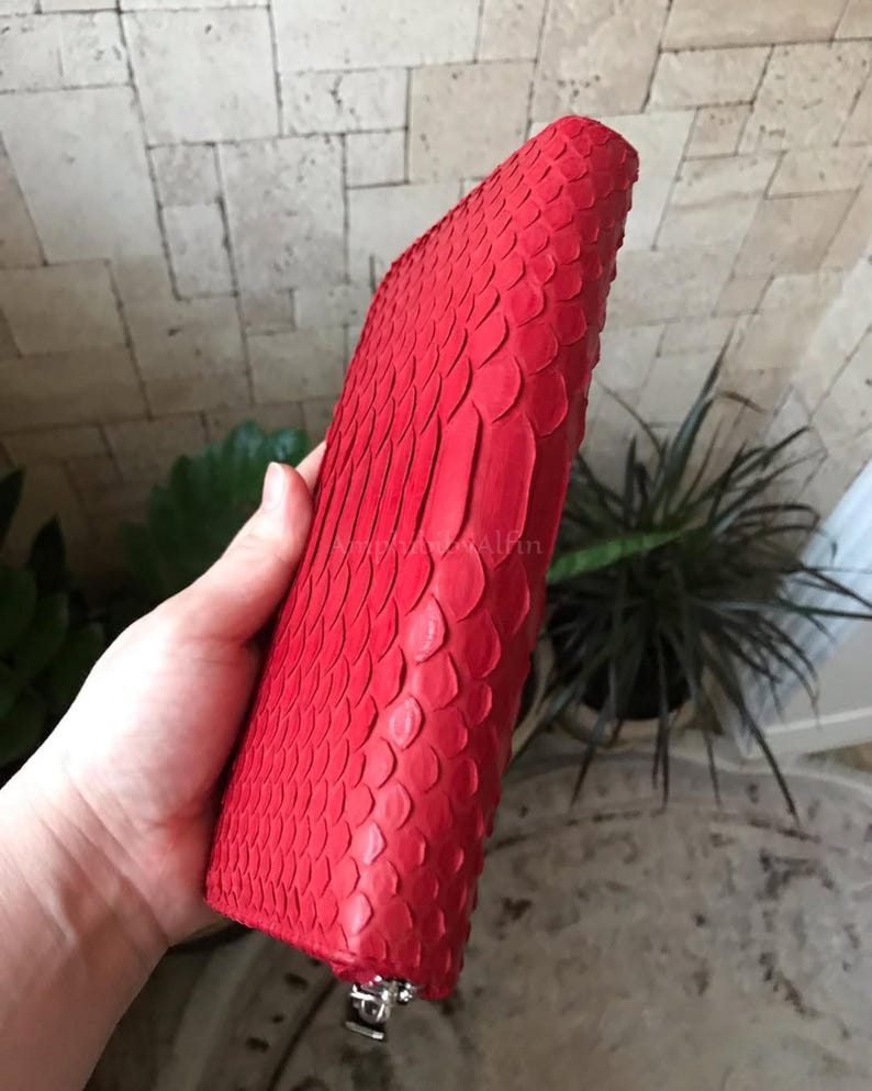 Peut inclure: Un portefeuille rouge vif pr&eacute;sentant un motif textur&eacute; en forme d'&eacute;cailles sur toute sa surface ext&eacute;rieure. Le portefeuille a une forme rectangulaire avec des bords arrondis et une tirette de fermeture &eacute;clair en m&eacute;tal argent&eacute; visible en bas.