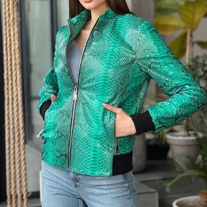 May include: A vibrant green jacket featuring a detailed black snakeskin pattern throughout. The jacket has a full-length silver front zip, a stand-up collar, and contrasting black ribbed cuffs and a black ribbed hem at the waist.