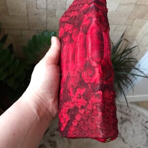 Peut inclure: Un portefeuille rouge vif pr&eacute;sentant une surface textur&eacute;e semblable &agrave; des &eacute;cailles. Le portefeuille a une forme rectangulaire avec des bords arrondis et une fermeture &eacute;clair visible en bas. La surface affiche des nuances de rouge vari&eacute;es.