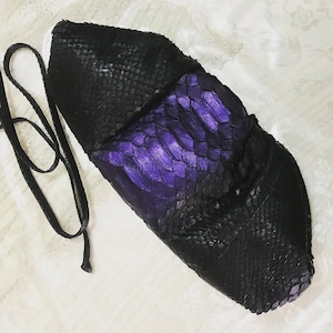 Könnte beinhalten: Eine strukturierte Handtasche mit einem strukturierten, schuppenartigen Muster in Schwarz und einem leuchtend violetten Mittelteil. Die Tasche verfügt über einen dünnen, passenden schwarzen Schulterriemen an der Seite und eine spitz zulaufende Form.