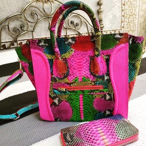 Può includere: Una borsa strutturata e un portafoglio rettangolare abbinato con un vivace motivo a pelle di serpente multicolore nei toni del rosa acceso, verde lime, turchese e rosso. La borsa presenta due manici, una tasca frontale con zip e pannelli laterali rosa.
