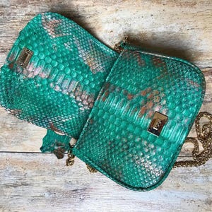 May include: A vibrant emerald green crossbody bag featuring a textured snakeskin pattern with metallic copper highlights. The rectangular bag includes a gold-tone metal clasp on the front flap and a matching gold-tone chain shoulder strap.