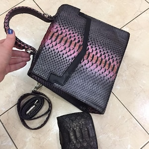 May include: A structured handbag with a textured snakeskin pattern in shades of dark grey, black, and iridescent purple, featuring a top handle, a detachable shoulder strap, and a matching small rectangular zippered wallet with a similar texture.