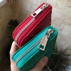 Peut inclure: Deux petites pochettes rectangulaires &agrave; fermeture &eacute;clair, l'une rouge vif et l'autre bleu sarcelle, pr&eacute;sentant toutes deux une texture en relief semblable &agrave; des &eacute;cailles. Chaque pochette est dot&eacute;e d'une tirette en m&eacute;tal argent&eacute;.