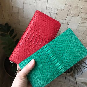 Peut inclure: Deux portefeuilles rectangulaires &agrave; fermeture &eacute;clair avec un motif textur&eacute; en peau de serpent. L'un est rouge vif et l'autre est vert &eacute;meraude &eacute;clatant. Les deux articles poss&egrave;dent une fermeture &eacute;clair m&eacute;tallique sur le dessus et le c&ocirc;t&eacute;.