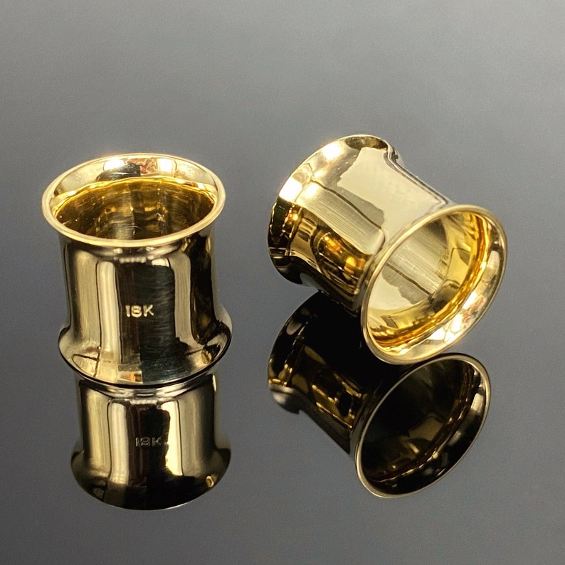 May include: Two gold-colored metal ear gauges, one with a slightly flared edge and the other with a smooth edge. Both gauges are marked with "18K".